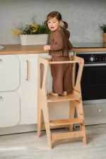 Bambina nella learning tower al bancone della cucina vista da dietro