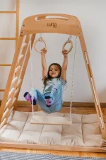Materassino imbottito beige sotto gli anelli della palestra Montessori in legno