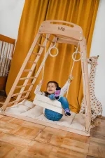 Bambina appesa agli anelli sopra il materassino beige della palestra Montessori