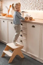 Bambina in piedi sullo sgabello a due gradini al bancone della cucina