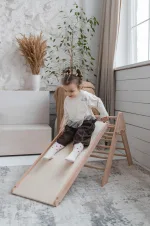 Bambino scivola sulla rampa del triangolo Pikler in soggiorno