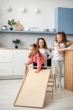 Due bambine giocano con il triangolo Pikler e lo scivolo in cucina