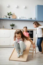 Bambina scende dallo scivolo del triangolo Pikler in cucina con la mamma