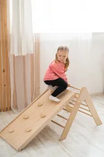 Bambina si arrampica sulla rampa con prese del triangolo Pikler