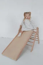 Bambina seduta in cima allo scivolo del triangolo Pikler in legno